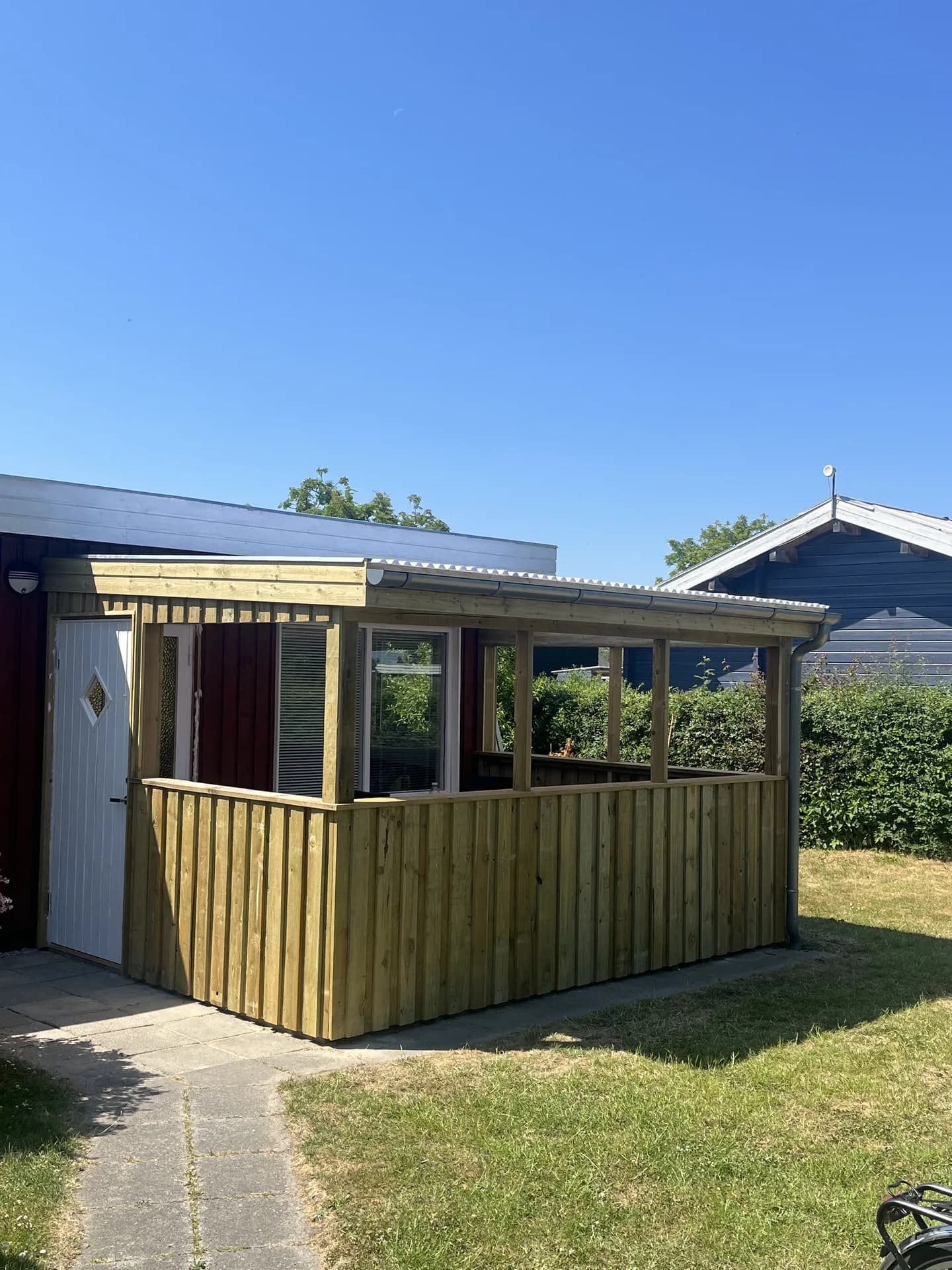 Overdækket terrasse med træstolper, rækværk og lys tagbeklædning