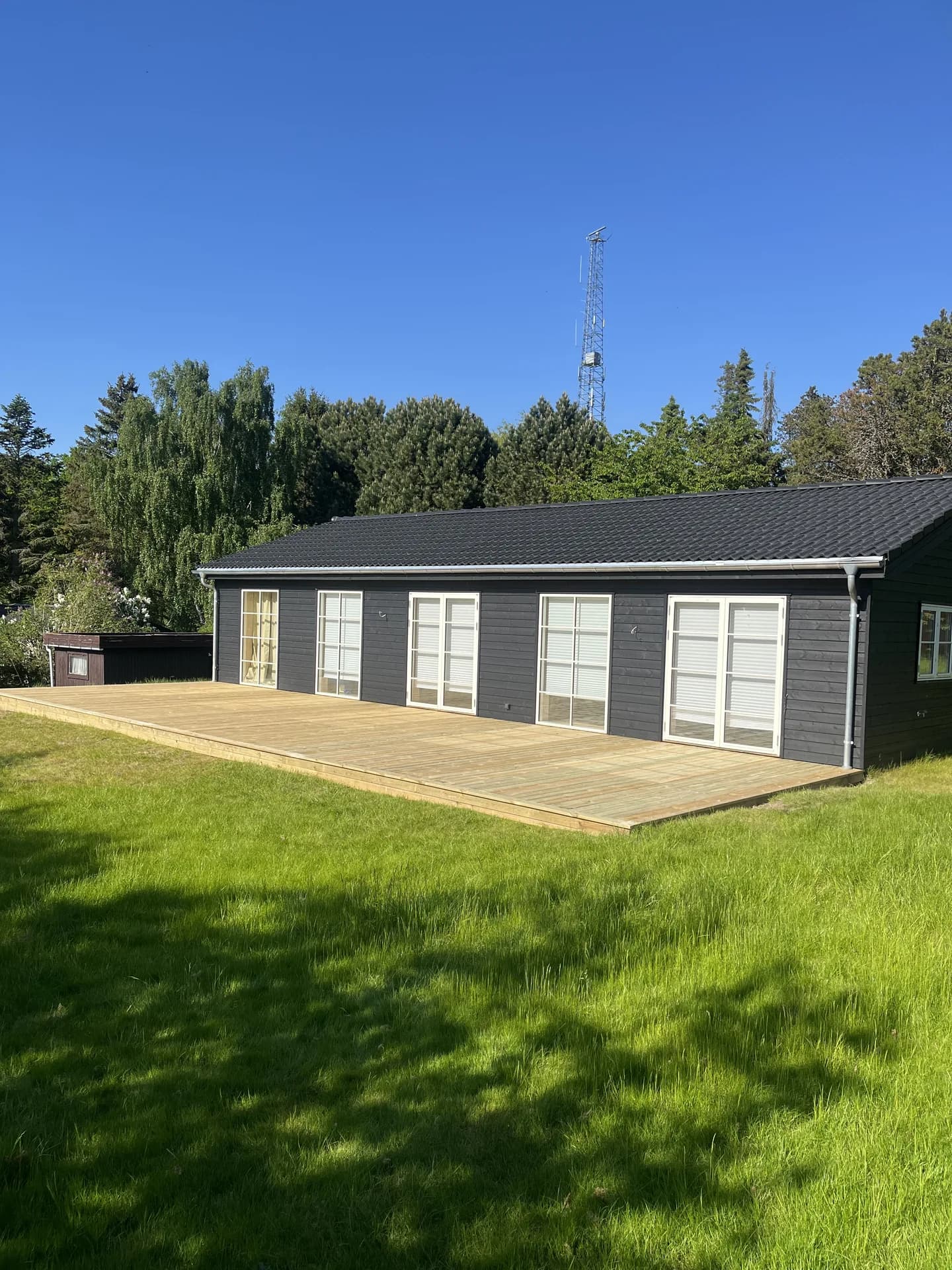 Træterrasse langs et mørkt sommerhus med hvide terrassedøre
