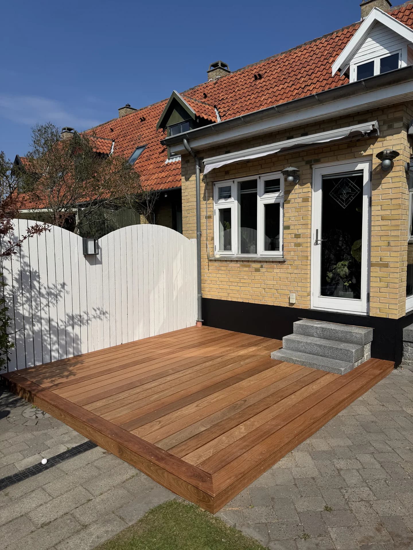Træterrasse med indrammet kant foran en gul murstensvilla